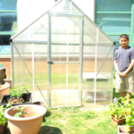 student standing next to greenhouse