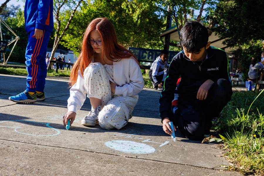 students writing with chalk on sidewalk