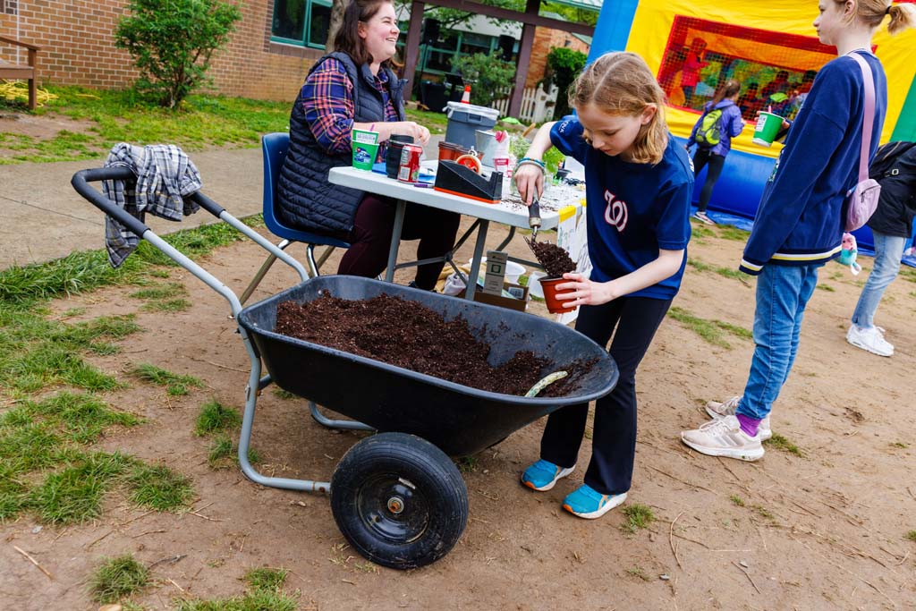 child scooping dirt from a wheelbarrow